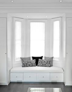 a window seat in the corner of a room with two pillows on it and some drawers below