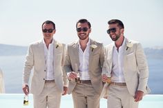 three men in suits and sunglasses standing next to each other holding champagne glasses, smiling at the camera