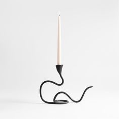 a black candle holder with a single white candle on it's end and a long black cord in the middle