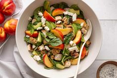 a white bowl filled with spinach, peaches and feta cheese next to apples