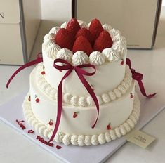 a three tiered cake with strawberries on top and ribbon around the edges, sitting on a table