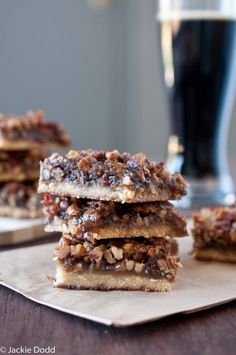 three pieces of pecan bar sitting on top of a piece of parchment paper next to a glass of beer