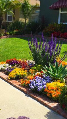 a flower garden in front of a house with lots of colorful flowers and greenery