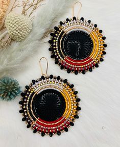 Gorgeous and elegant colours of black, yellow, dark red, white pearl, coordinating delicas, and light metallic gold beads were used to create these Indigenous made XL medicine wheel beaded earrings. Accented with a large black cabochon and a dainty row of rhinestones and gold banding around the beadwork that has the delica beads wrapped around it. The beautiful border is completed in black rondelle beads and metallic gold beads. These earrings measure approx. 2.76x2.75" and hang approx. 3.25" Th Elegant Colours, Medicine Wheel, Beaded Wraps, Delica Beads, White Pearl, Gold Beads, Metallic Gold, Gold Bands, Large Black