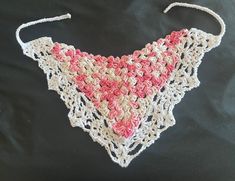 a crocheted pink and white triangle on a black cloth with two strings attached to it