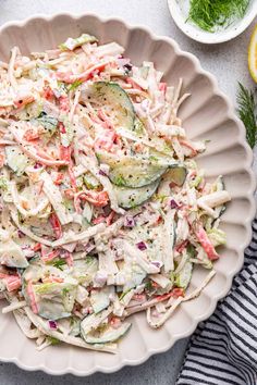 a white bowl filled with coleslaw and cucumbers next to lemon wedges