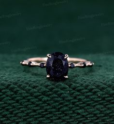 a ring with a blue stone on it sitting on a green cloth in front of a black background