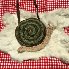 a crocheted snail purse laying on top of a red and white checkered table cloth