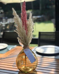 a vase with some flowers in it sitting on a wooden table outside near plates and utensils