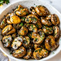 a white bowl filled with mushrooms covered in seasoning and sprinkled with parsley