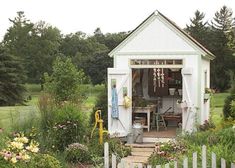 a small white shed sitting in the middle of a garden filled with lots of flowers