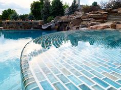 an outdoor swimming pool surrounded by rocks and water features a slide in the back ground