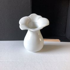 a white vase sitting on top of a table next to a black box with a pencil in it