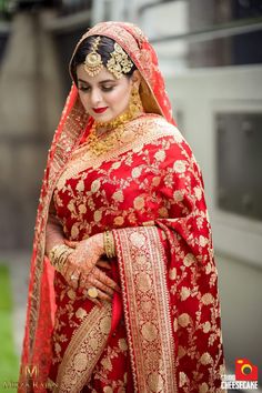 a woman in a red and gold bridal outfit with her hands on her hips