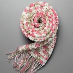 a pink and white crocheted scarf with fringes on top of a gray surface