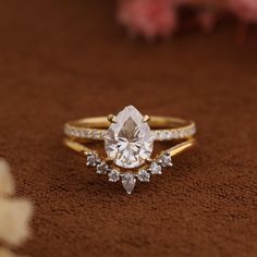 a close up of a diamond ring on a brown surface with flowers in the background