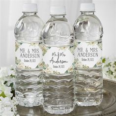 three water bottles sitting on top of a metal tray next to white and pink flowers