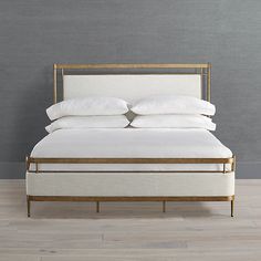 a bed with white linens and gold frame against a gray wall in a bedroom