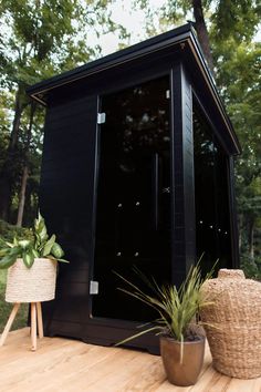 a small black building sitting on top of a wooden deck next to a potted plant