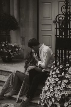 a man and woman sitting on the steps in front of a building kissing each other