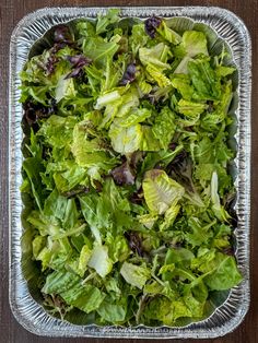 lettuce is in a metal container on a wooden table, ready to be eaten