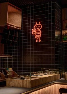 a neon sign above a counter in a restaurant with black tiled walls and wooden counters