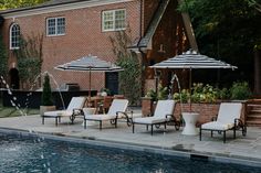 an outdoor pool with lounge chairs and umbrellas next to the swimming pool in front of a brick building