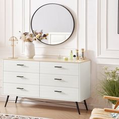 a white dresser with a mirror and vase on it in front of a wall mounted plant