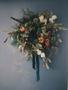 an arrangement of flowers and foliage on a blue wall