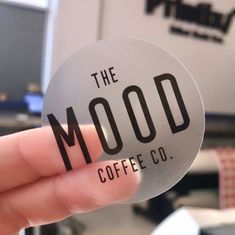 a person holding up a sticker that says the mood coffee co in black and white