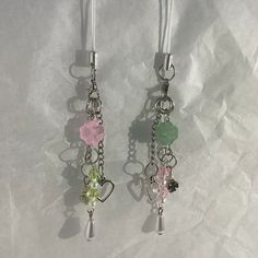 two pairs of earrings with charms attached to them on a white surface, one has a heart and the other is a flower