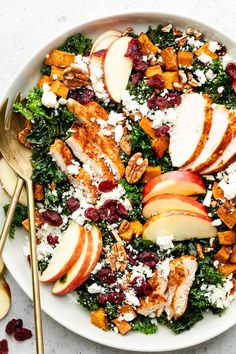 a white plate topped with chicken, apples and cranberries next to gold spoons