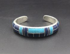 This is a heavy duty sterling silver cuff bracelet made with inlaid natural turquoise and natural lapis lazuli stone. The width is 12mm, tapering to 8mm. The thickness is 6 mm. The gap is 1.25 inches for a man's wrist size; 1 inch for a woman's wrist size. Select your wrist size from the drop down menu, and we will make your bracelet to fit. Please measure your wrist size if you are unsure of the size. Solid sterling silver and stone inlay bracelets cannot be changed. No returns are accepted unl Adjustable Blue Engraved Cuff Bracelet, Artisan Blue Cuff Bangle Bracelet, Artisan Blue Bangle Cuff Bracelet, Southwestern Engraved Blue Cuff Bracelet, Artisan Engraved Blue Bracelets, Artisan Blue Engraved Cuff Bracelet, Adjustable Blue Cuff Bracelet With Inlay, Southwestern Sterling Silver Cuff Bracelet In Blue, Blue Polished Bangle Cuff Bracelet