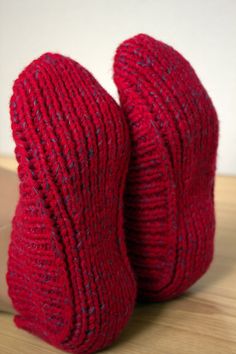 pair of red knitted slippers sitting on top of a wooden table next to a white wall