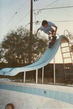 a man riding a skateboard down the side of a slide in a swimming pool