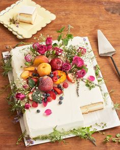 a cake with flowers and fruit on it sitting on a table next to a knife