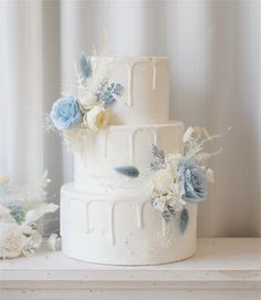 a three tiered white wedding cake with blue and white flowers