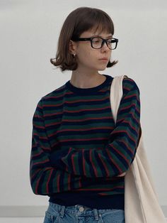 a woman wearing glasses and a striped sweater is standing with her arms folded in front of her chest