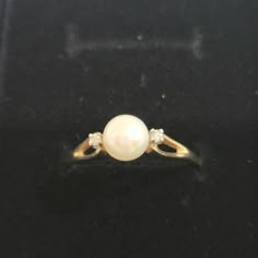 a pearl and diamond ring sitting on top of a black surface