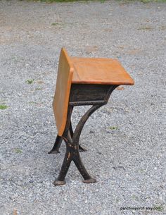 an old school desk sitting on top of a wooden bench in the middle of gravel