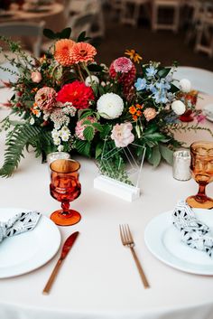 the table is set with plates, silverware and floral centerpieces on it