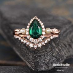 an emerald and pearl ring on top of a piece of wood with pearls around it