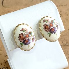 "♥Vintage clip on earrings oval shaped with a white front and multi colored flowers and foliage with a \"sugared\" surface. These pre-owned and signed \"Germany\" earrings are in great condition and measure 13/16\" x 3/4\". Fancy them for yourself or as a gift for a special someone whom you know will adore and treasure these earrings from the past. Enjoy! Stand out from the crowd just a little bit more by purchasing and wearing an adornment that is uncommon, unique, and perhaps one of a kind when it comes to antique, vintage, and handmade creations, and repurposed or upcycled jewelry and accessories. To see more Clip on vintage earrings in my shop, please click here: https://www.etsy.com/shop/JulesBaublesandMore?ref=seller-platform-mcnav&section_id=35062758 Before departing, please have a Handmade Vintage White Clip-on Earrings, Vintage White Oval Earrings, Violet Rose, Multi Colored Flowers, Flowers Purple, Colored Flowers, Reflective Material, Dog Teeth, Upcycled Jewelry