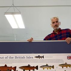 a man standing behind a sign with fish on it's display board in front of him