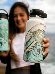 a woman holding two water bottles in front of the ocean