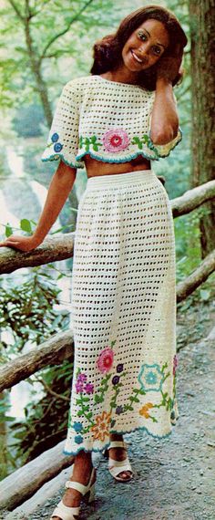 a woman in a crochet dress standing on a bridge with her arms behind her head