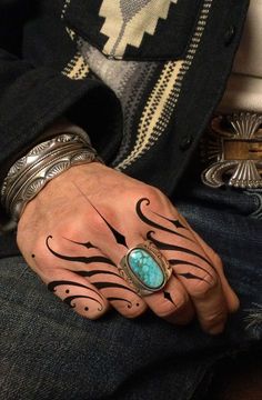 a man's hand with tattoos on it and a turquoise stone in the middle