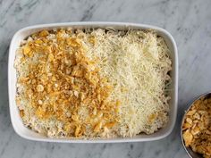 a casserole dish with cheese and bread crumbs next to a metal bowl