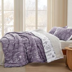 a bed in a bedroom with purple and white comforter on top of the bed