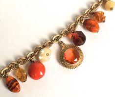 an orange and white bracelet with charms on it's sides, hanging from a gold plated chain